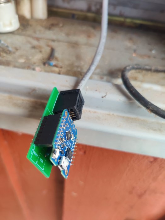 D1 mini mikrokontroller monterad på en grön PCB ovanför en träyta, med vit kabel ansluten.