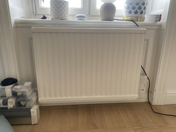 Radiator i vit nisch ovanpå ett trägolv med dekorativa föremål på fönsterbrädan.