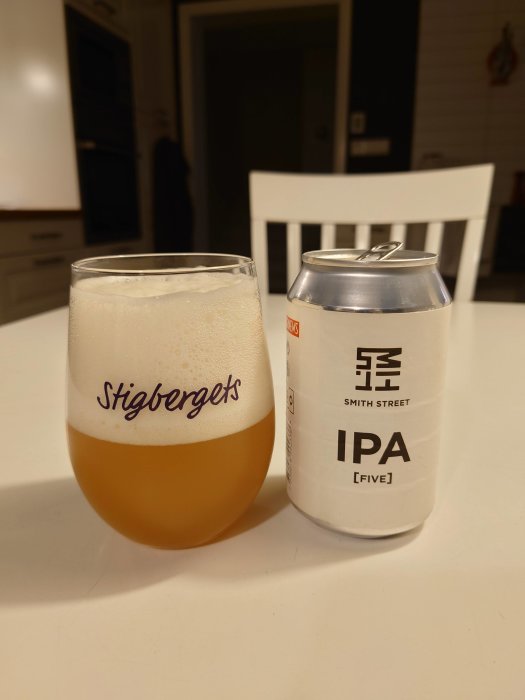 Ett glas öl med skum och en ölburk märkt "IPA" på ett köksbord.