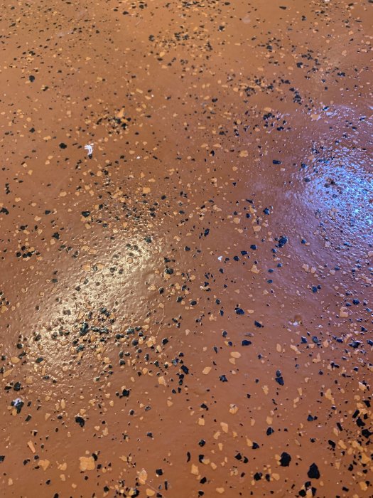 Gammalt källargolv med orange-brun färg och svarta samt beige fläckspridningar, inga tecken på färgsläpp.