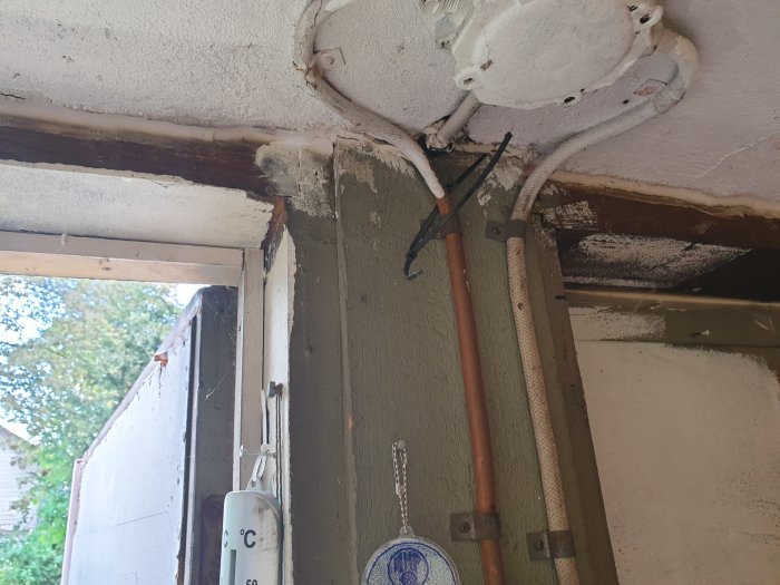Hörnet av ett källargarage med synlig pelare och balk, ledningar och en gammal portöppning.