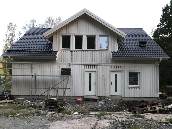 Nybyggt hus med grundmålad fasad, ställningar och utspridd byggmaterial runtomkring.