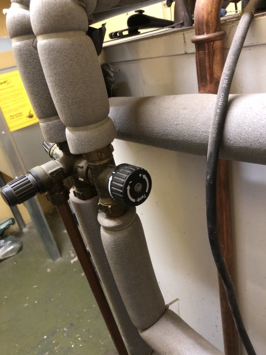 Insulation-wrapped pipes with a valve and setting dial, part of a pellet boiler system.