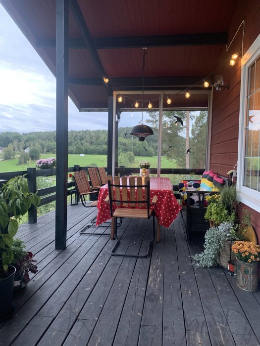 Altan med röda väggar och svart golv, möblerad med ett bord och stolar, intill en svart stolpe, lämplig för väggmonterad terrassvärmare.