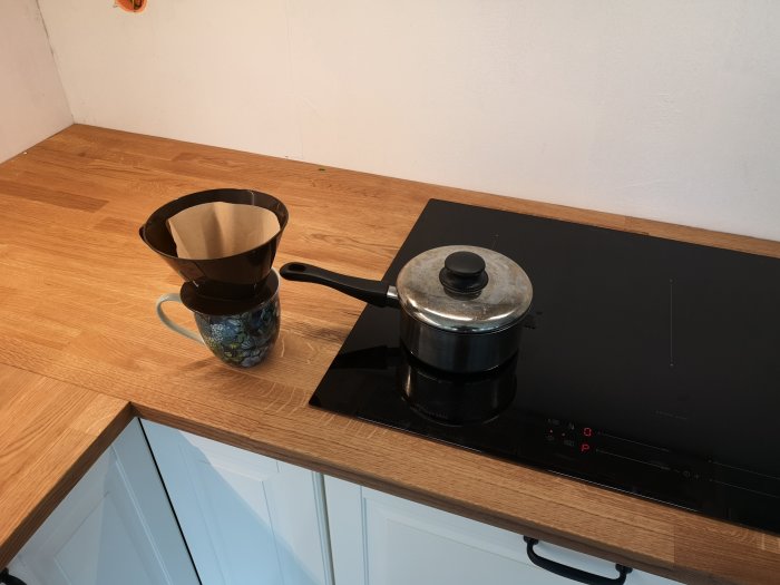 Nyligen installerad spishäll med kastrull och kaffebryggare på ett köksbänk i trä.