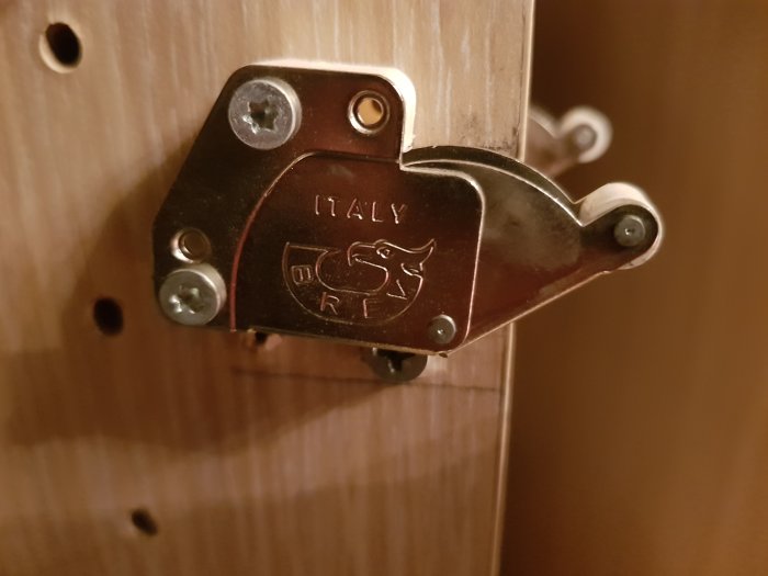 Metalldörrstängare märkt "ITALY" monterad på träyta, sökes av användare i Frankrike.