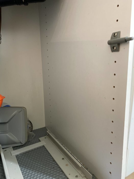 Interiör av köksskåp med Blum-gångjärn och hyllstödspinnar, grått skåpinsida.