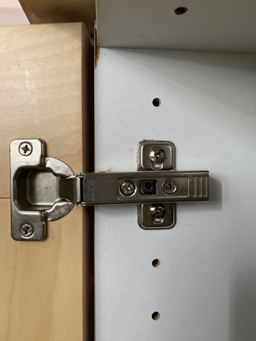 Närbild på ett Blum-märkt köksluckgångjärn monterat på en vit lucka med synlig kant av trä.