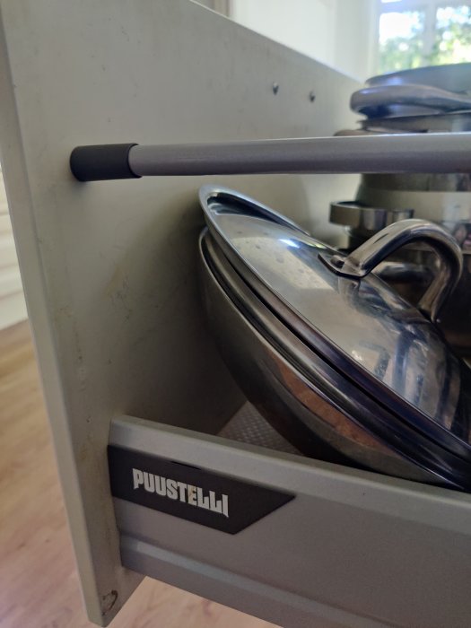 Luckinsats med handtag och märkning "PUUSTELLI" i ett köksskåp med krukor och lock.