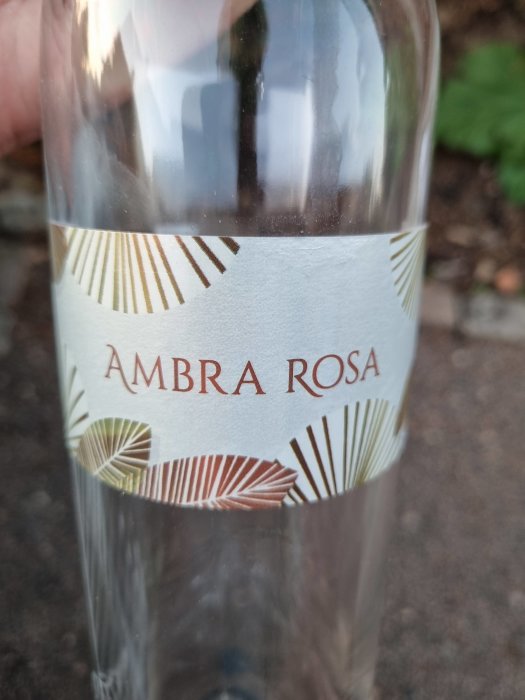 Närbild av en tom vinflaska med etiketten "AMBRA ROSA" och dekorativa mönster.