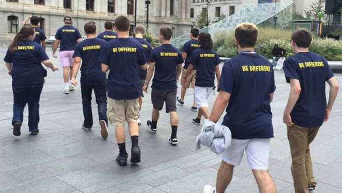 Grupp människor i matchande t-shirts med texten "BE DIFFERENT" som går utomhus.