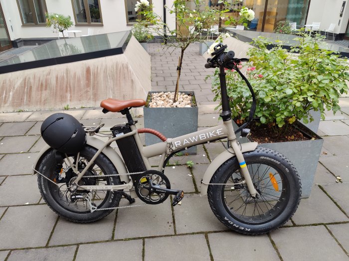 Elektrisk cykel med tjocka däck och hjälm parkerad utomhus.