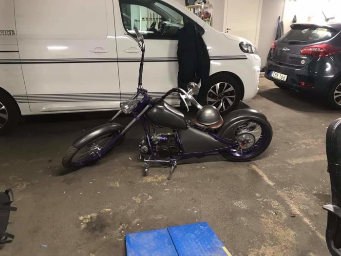 Custombyggd låg motorcykel med högt styre parkerad i ett garage.