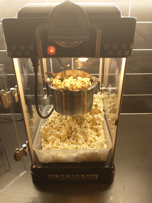 Retrostil popcornmaskin i drift full med nygjord popcorn i ett kök.