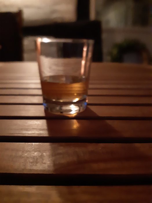 Ett glas Glenfiddich whisky på ett träbord i suddig bakgrund.