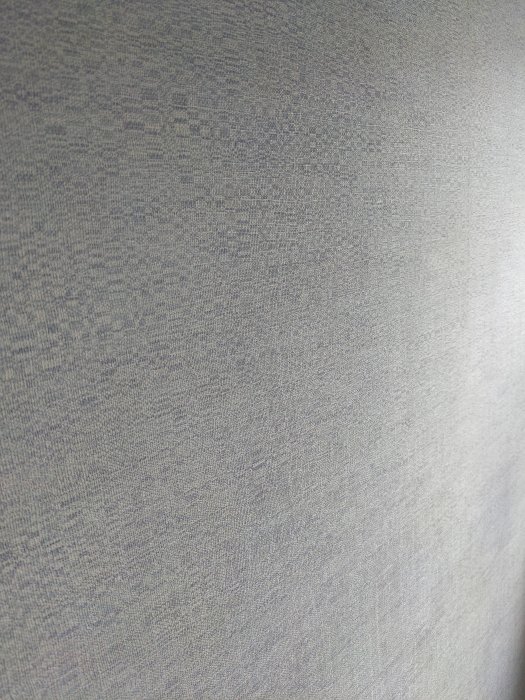 Närbild av en grå strukturerad tapet, som kan vara gjord av papper, på en vägg som ska renoveras.