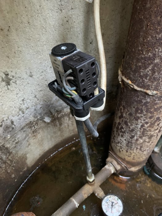 Tryckströmbrytare och rör anslutna till brunnen med en tryckmätare, synliga kablar och korrosion.