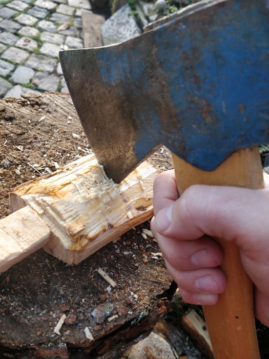 En hand som håller i en yxa för att forma en sked av trä på en stubbe.