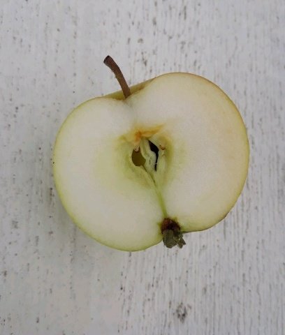 Halverat äpple med synliga kärnhus och frön på en vit bakgrund.