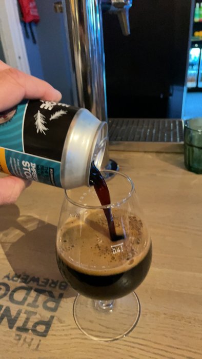 Hällning av mörk stout i ett glas på pub, ofiltrerat öl från Falkenberg.