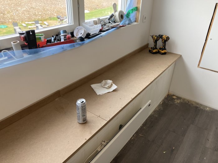 Byggmaterial och verktyg utspridda på bänk i ett hus under konstruktion.