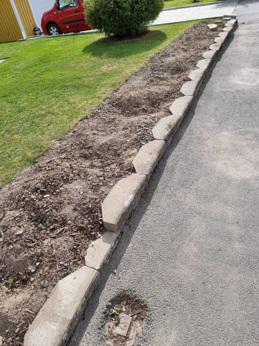 Rad av halvt borttagna betongstenar vid trottoarkant med gräsmatta och jord i bakgrunden.