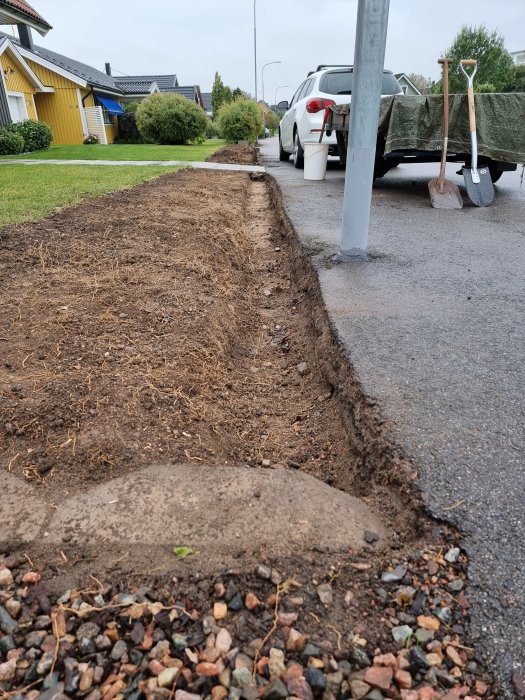 Uppgrävd stödmursplats längs gata med borttagna stenar och synlig sättsand, verktyg i bakgrunden.