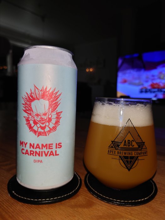 Burk med etikett "My Name is Carnival DIPA" och ett glas dubbel IPA på ett bord med suddig TV i bakgrunden.