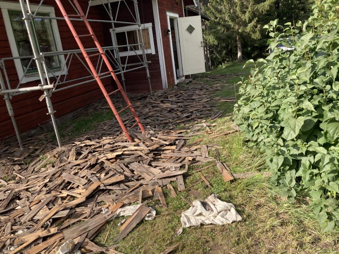 Röda trähus med stegar intill, högar av rivet träspån på marken och en vit trasa.