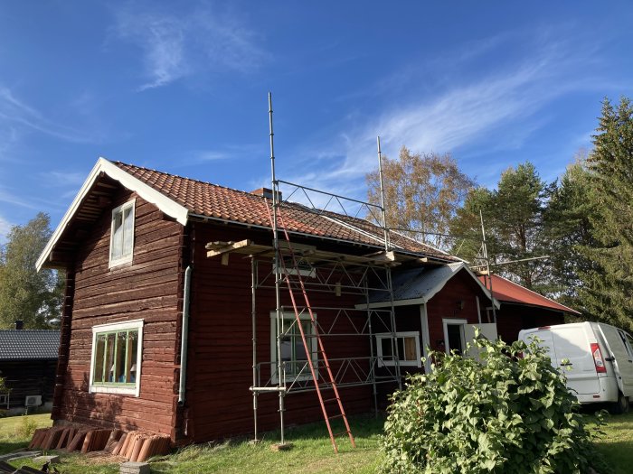 Renovering av rött trähus med nytt tak och ställningar runt byggnaden under en klar himmel.