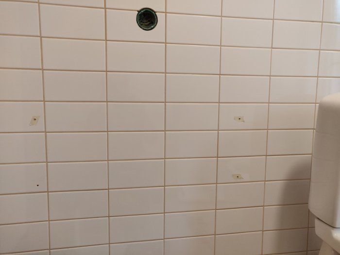 Kaklad vägg med synliga fästhål och eluttag nära ett toalettstolshörn.