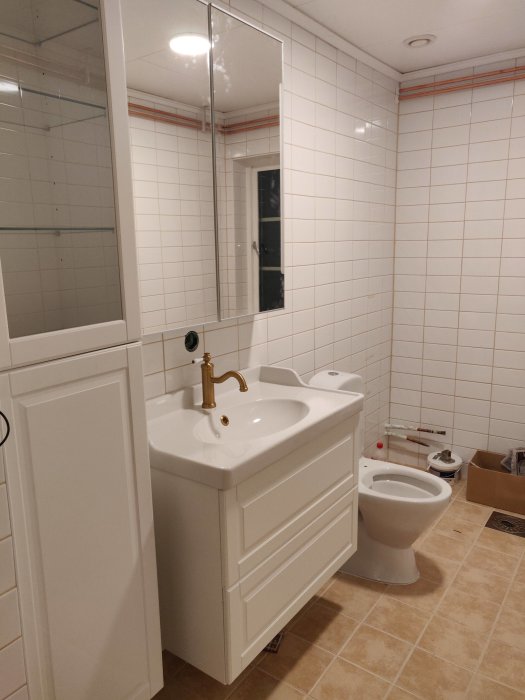 Renoverat badrum med vit kommod, handfat, spegelskåp, toalett och kaklade väggar.
