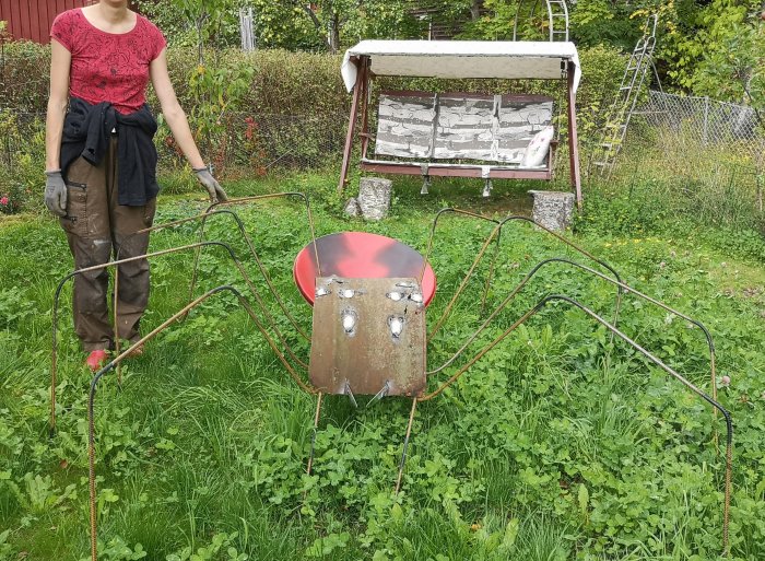 Person visar ett svetsat spindel-pynt inför Halloween i trädgården.