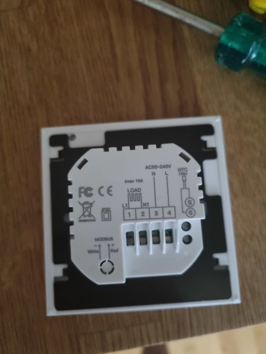 Otydlig bild på en termostat för golvvärme med märkningen AC95-240V och anslutningsterminaler, intill en skruvmejsel.