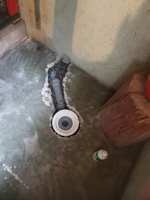 Ett rör som sticker ut från ett betonggolv i ett pannrum, omgivet av ojämnt gjuten massa och en sprayburk.
