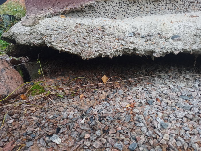 Erosion under betongplatta med synligt hålrum och grus runt, behov av åtgärd för avrinning.