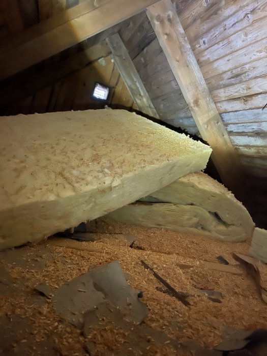 Isolering med sågspån och stenull på kallvindsgolvet i äldre hus, potentiella fuktskador.