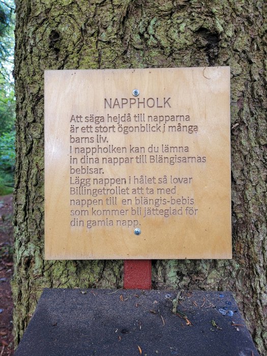 Skylt med text om "napphålk" monterad på ett träd i skogen.