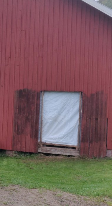 Röd ladugårdsvägg med delvis öppnad sektion täckt av plast, markerad för garageöppning.