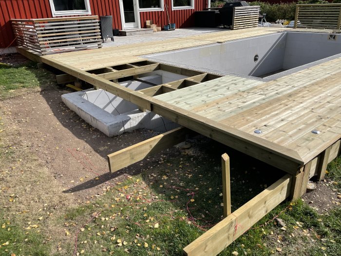 Trädäck i konstruktion vid hus med delvis installerade trallbrädor och en oavslutad trappa.