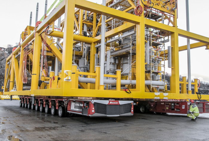 Specialtransport av stor gul industriell konstruktion på fleraxlad släpvagn med arbetare bredvid.