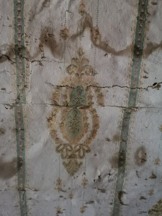 Sliten och gammal tapet med klassiskt mönster och fläckar på en vägg som behöver renovering.