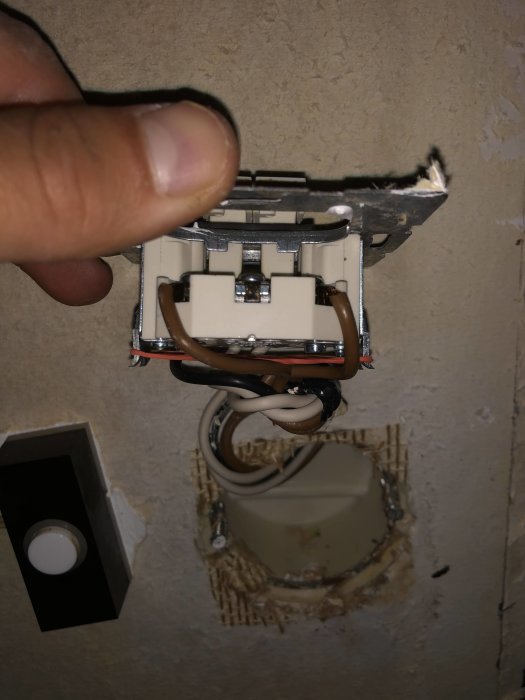 Eluttag och kablar syns i öppet väggutrymme, hand håller i en dubbelkopplad strömbrytare.