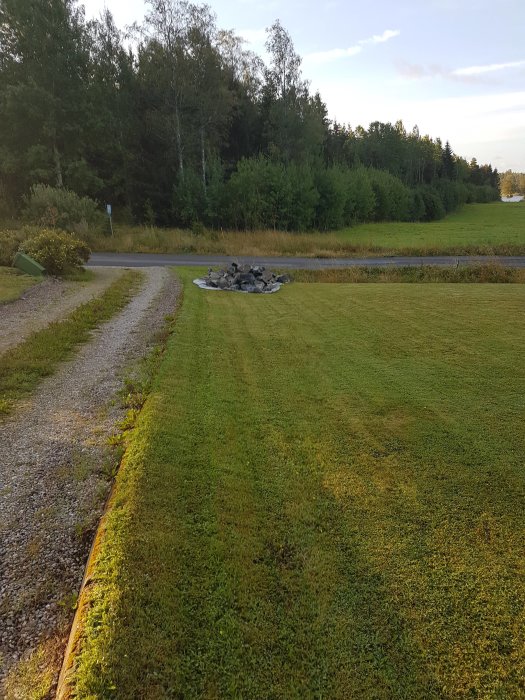 Stenar på markduk i trädgård, resultat av spräckning med kilar, omgiven av gräsmatta och skog.