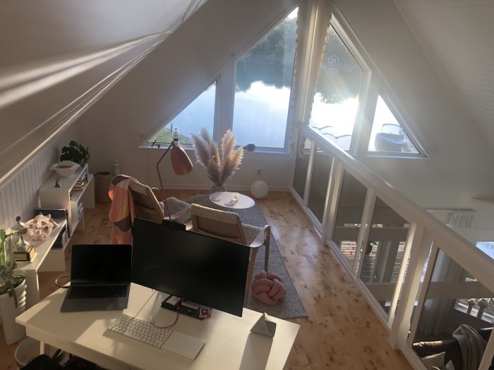 Soligt hemkontor med utsikt över vatten och båt genom fönster, skrivbord med datorskärm, vitt interiör.