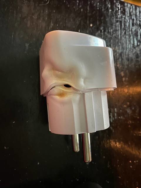 Smält och deformerad vit elkontakt mot en mörk bakgrund.