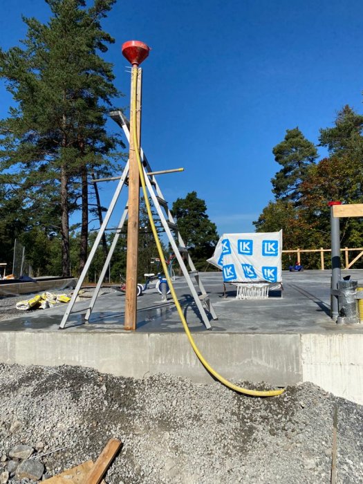 En improviserad trattuppsättning för betongarbete med en stege och buntband på en byggplats.