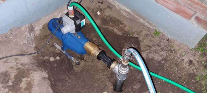 En vattenpump med anslutna slangar och rör nere på 5 meter i ett grävt hål, indikerar färdigställande av rörinstallation.