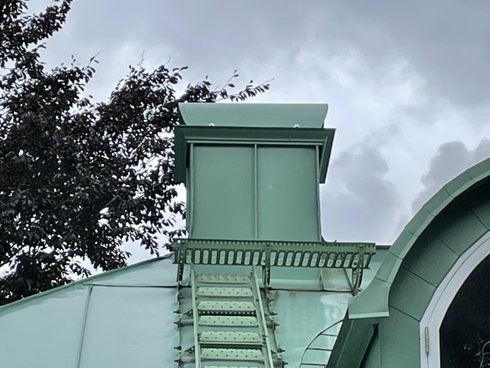 Nymålad skorsten i grönt på ett nytt tak mot en molnig himmel.