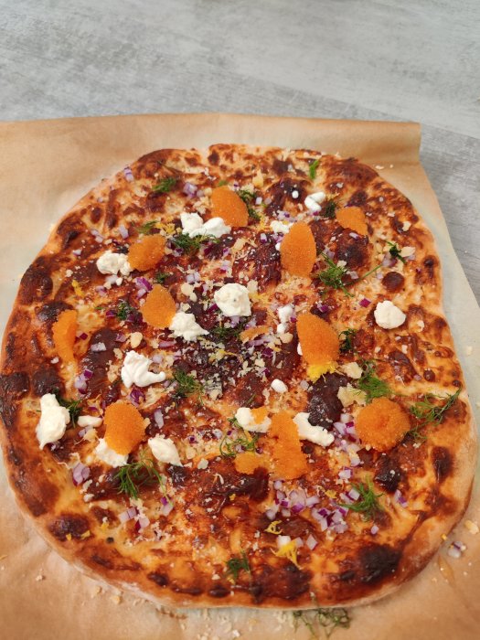 Hembakad läjromspizza med vita ostklumpar, lök och dill på bakplåtspapper.